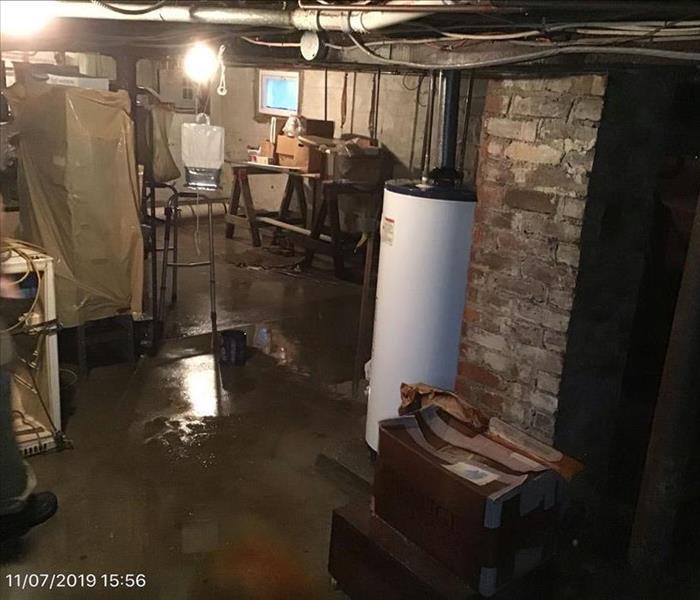 murky water puddles in a basement with infrastructure appliances and a workbench