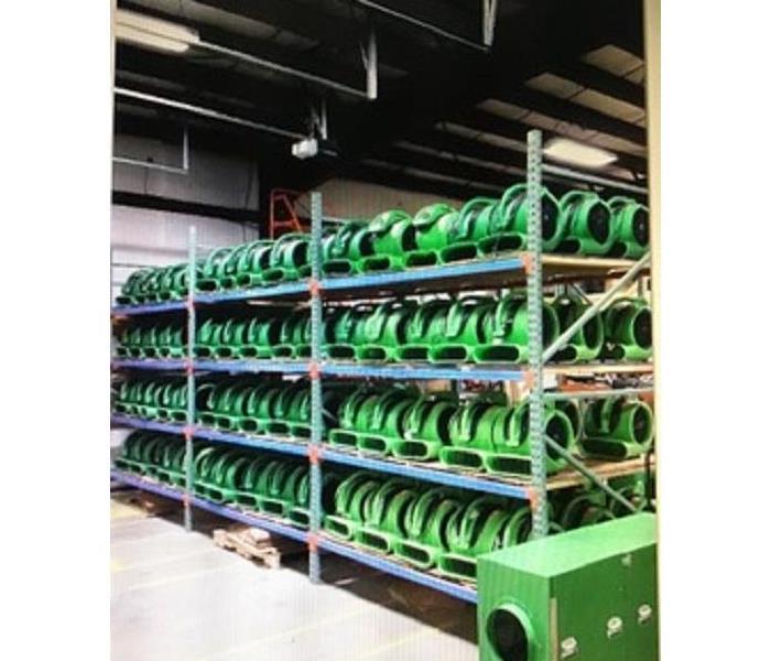 Multiple large four-tier metal shelves packed with SERVPRO air movers in a clean warehouse space