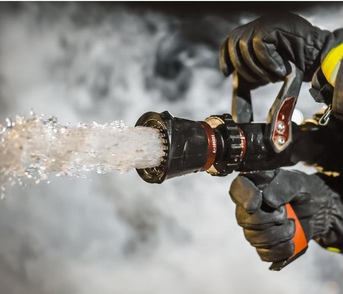 Closeup of fireman holding fire hose; water coming from hose